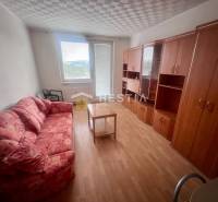 Szoba egy háromszobás lakásban kanapéval, szekrényekkel és asztallal a világos padlón.