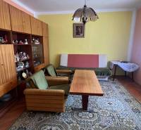 Nappali egy családi házban retro bútorokkal, zöld fotelekkel és nagy szőnyeggel.