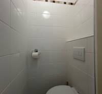 Fürdőszoba egy egyszobás lakásban fehér csempékkel és dekoratív csíkkal ellátott fallal.