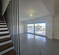 Nappali a villában modern lépcsőkkel és nagy ablakokkal.