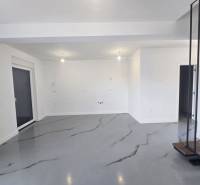 Priestranná miestnosť vo Vile s bielymi stenami a šedou podlahou s dekorom.