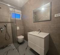 Fürdőszoba a villában WC-vel, zuhanyzóval és mosdóval, kőmintás csempével.