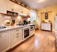 Konyha egy kétszobás lakásban fa mintázatú padlóval, világos konyhabútorral és növényekkel.