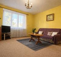 Nappali egy kétszobás lakásban, sárga falakkal, szőnyeggel és bútorokkal.