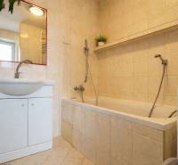 Fürdőszoba egy kétszobás lakásban káddal, mosdóval, tükörrel és bézs csempével.