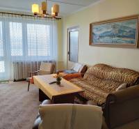 Nappali kanapéval, fotellel és asztallal egy kétszobás lakásban nagy ablakkal.