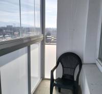 Üvegezett erkély kilátással és műanyag székkel, egy 2 szobás lakás része.