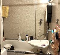 Fürdőszoba egy kétszobás lakásban káddal, mosdóval és burkolt falakkal.