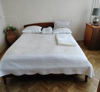 Hálószoba franciaággyal, fa mintázatú padlóval és éjjeliszekrénnyel egy kétszobás lakásban.