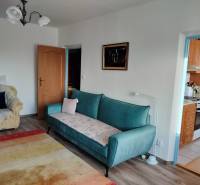 Nappali egy kétszobás lakásban kanapéval és fotellel, fa dekoros padlóval.