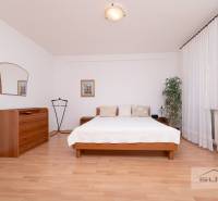 Hálószoba ággyal, komóddal és fa dekorációjú padlóval egy háromszobás lakásban.