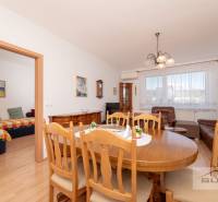 Étkezőasztal fa székekkel egy háromszobás lakásban, mellette a nappali.