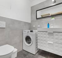 Fürdőszoba mosógéppel és mosdóval, csempe, fiókos szekrény, tükör egy egyszobás lakásban.