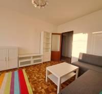 Nappali fehér szekrényekkel, szürke kanapéval és fa mintázatú padlóval egy kétszobás lakásban.