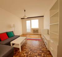 Nappali egy kétszobás lakásban kanapéval, fehér bútorokkal, színes párnákkal és fa dekorációjú padlóval.