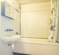 Fürdőszoba káddal és zuhanyfüggönnyel egy kétszobás lakásban, világos falak, narancssárga padló.