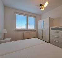 Hálószoba egy kétszobás lakásban fehér bútorokkal és ággyal, ablak redőnyökkel.