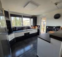 Konyha egy családi házban kerámia padlóval, sötét bútorokkal és nagy ablakokkal.