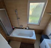 Fürdőszoba családi házban káddal és ablakkal, barna csempével burkolva.