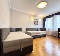 Szoba egy négy szobás lakásban két ággyal, légkondicionálóval és fa dekor padlóval.