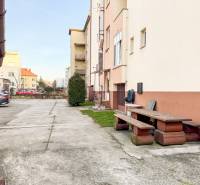 Parkolás és pad az épület előtt a Hodžova utcában, Trencsénben, közel egy 2 szobás lakáshoz.