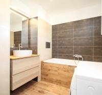 Fürdőszoba világos csempékkel, mosógéppel és fa dekoros padlóval egy kétszobás lakásban.