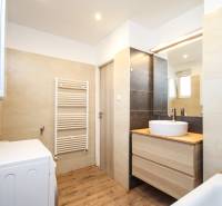 Fürdőszoba egy kétszobás lakásban mosdóval, tükörrel, mosógéppel és fa hatású padlóval.