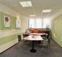 Irodák íróasztallal, székekkel, falakon elhelyezett dekorációkkal és ablakkal, függőleges redőnyökkel.