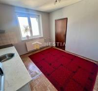 A háromszobás lakás konyhája szőnyeggel, fa dekor padlóval és egyszerű berendezéssel.