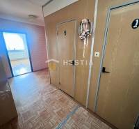 Folyosó egy 3 szobás lakásban, fa mintázatú padlóval és díszes koszorúval az ajtón.