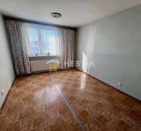 Szoba egy háromszobás lakásban, fa dekoros padlóval és világosszürke falakkal.