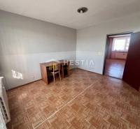 Szoba egy háromszobás lakásban, fa mintázatú padlóval és egyszerű íróasztallal.