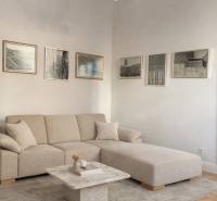 Nappali egy háromszobás lakásban bézs kanapéval, asztallal, képekkel és fa dekorációjú padlóval.