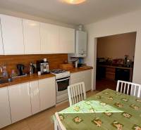 Konyha családi házban fehér szekrényekkel, fa dekorációval és étkezőasztallal.