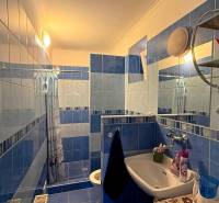 Fürdőszoba egy családi házban kék-fehér csempékkel, mosdóval és zuhanyzóval.