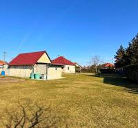 Gyepes telek családi ház mellett Zemianska Olčán, néhány házzal és bokorral.