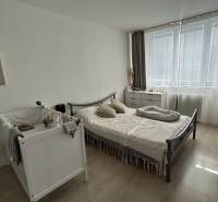 Hálószoba egy kétszobás lakásban kisággyal, ággyal és komóddal, fa mintázatú padlóval.