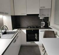 Konyha fehér szekrényekkel és asztallal egy kétszobás lakásban, fa dekoros padlóval.