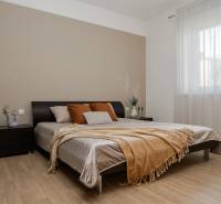 Hálószoba egy kétszobás lakásban, fa mintázatú padlóval, nagy ággyal és finom függönnyel ellátott ablakkal.