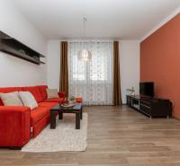 Nappali narancssárga kanapéval, polcokkal és fa dekorációjú padlóval egy kétszobás lakásban.