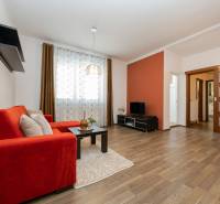 Nappali egy kétszobás lakásban kanapéval, TV-vel, fa dekoros padlóval és dekoratív függönyökkel.