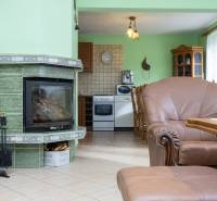 Családi ház belső tere kandallóval, ülőgarnitúrával és konyhasarokkal természetes árnyalatokban.