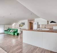 Nappali konyhával, zöld kanapé, fehér bútor, fa dekoros padló.