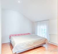 Hálószoba családi házban nagy ággyal és fa mintázatú padlóval.