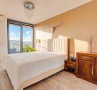 Hálószoba egy háromszobás lakásban ággyal, komóddal, dekorációkkal és fa mintázatú padlóval.