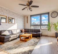 Nappali egy háromszobás lakásban bőrkanapéval, fa mintázatú padlóval és nagy ablakokkal.