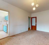 Nappali egy kétszobás lakásban szőnyeggel és fa bútorokkal, nyitott ajtó a konyhába.