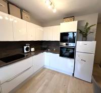 Konyha egy kétszobás lakásban fehér szekrényekkel, készülékekkel és fa mintázatú padlóval.