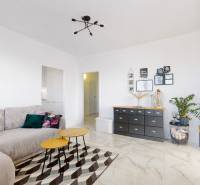 Nappali kanapéval és dekoratív bútorokkal egy háromszobás lakásban, fa mintázatú padlóval.