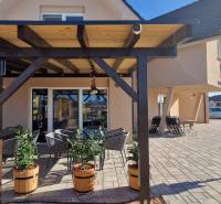 Újfalusi vendéglátóhely pergolával, virágládákkal és kültéri ülőhellyel a burkolaton.